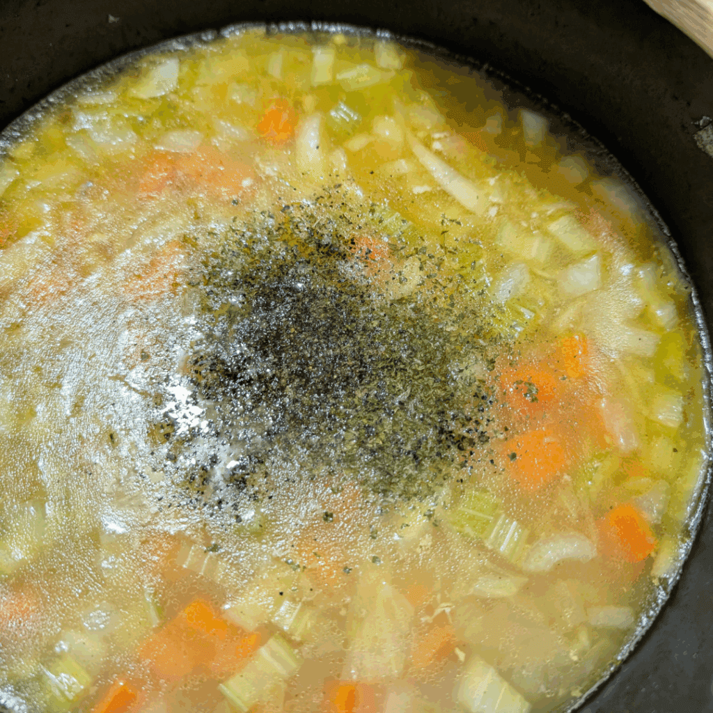 Seasoned vegetable soup simmering in a pot, raw ingredients like carrots and celery visible.
