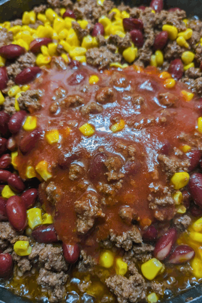 Ground beef with kidney beans, corn, and tomato sauce in a skillet.