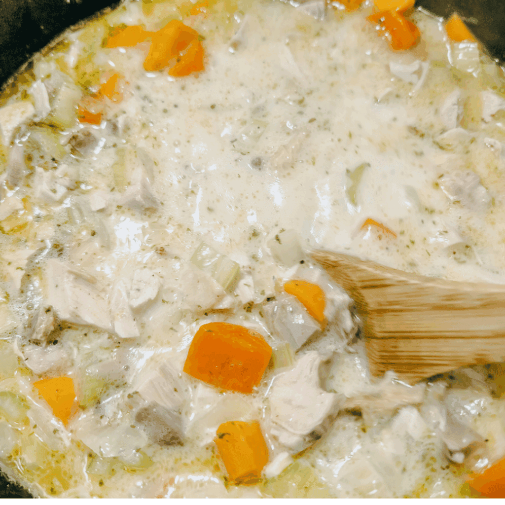 Creamy chicken and veggie soup cooking in a pot with a wooden spoon, perfect for comfort food recipes.