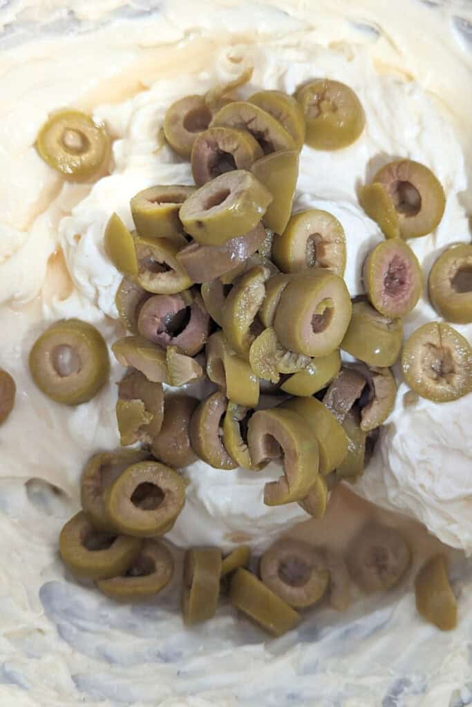 adding olives to cream cheese and mayonnaise dip