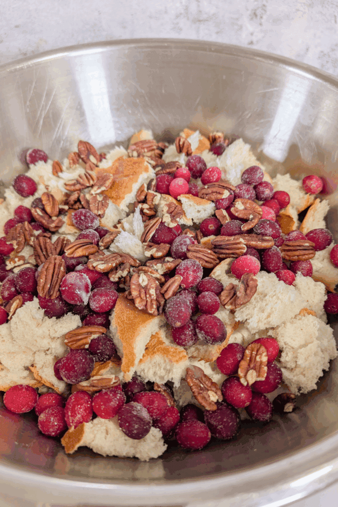 Fresh bread crumbs, frozen cranberries, and chopped pecans in a mixing bowl for holiday baking.