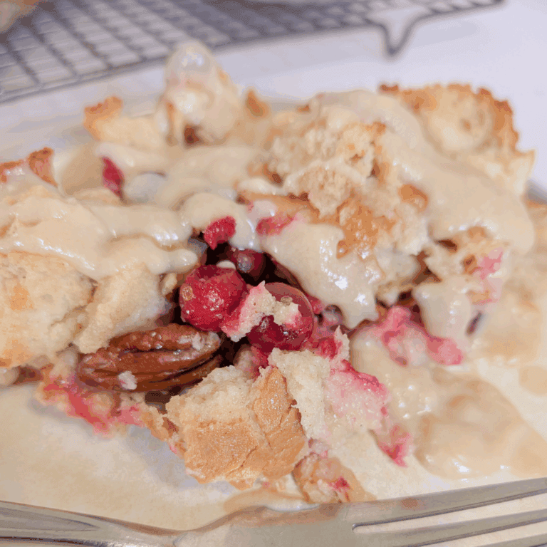 Butterscotch pecan cranberry dump cake with creamy topping on a plate.