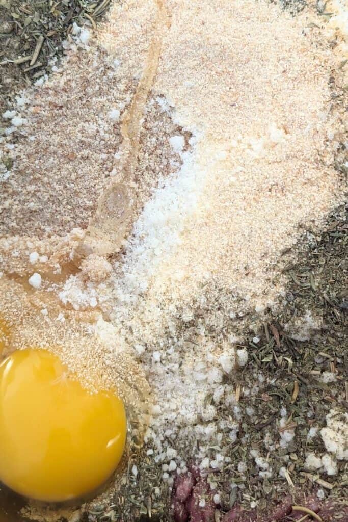 adding eggs and herbs to hamburger mix