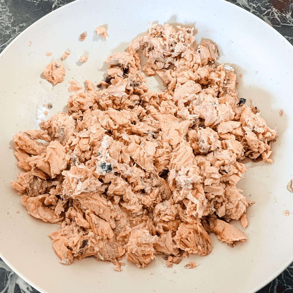 Canned tuna flakes in a white bowl, ready for cooking or salad preparation.