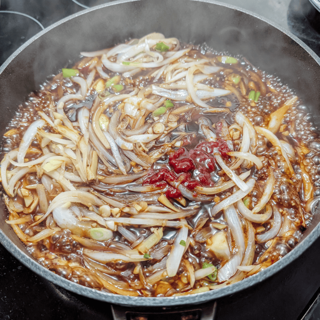 Sizzling Japanese beef rice bowl with onions and sauce in a skillet.