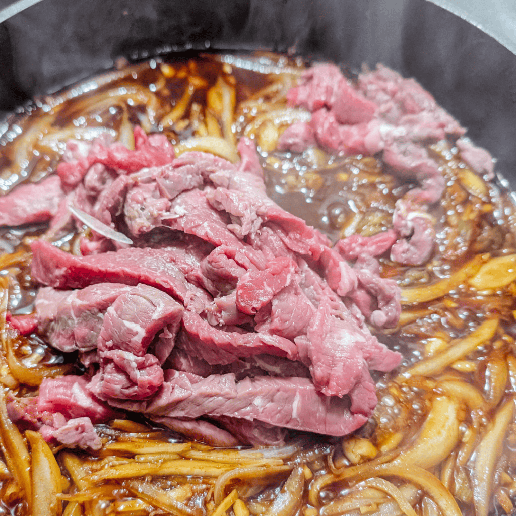 Beef cooking in a savory sauce with onions for Gyudon, a popular Japanese rice bowl dish.