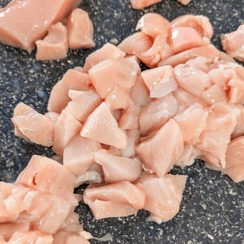 Diced cooked chicken for BBQ chicken wraps on a black surface.
