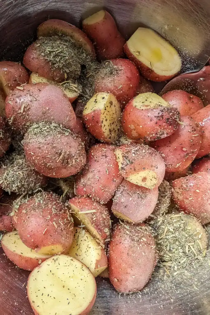 adding Italian herbs and pepper to potatoes in bowl