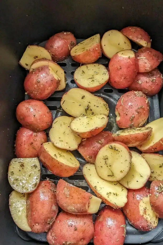 adding tossed herbed oiled potatoes into air fryer basket