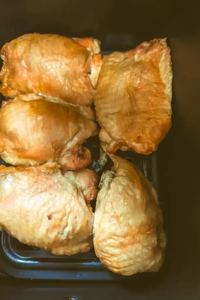 partially cooked chicken thighs in air fryer basket