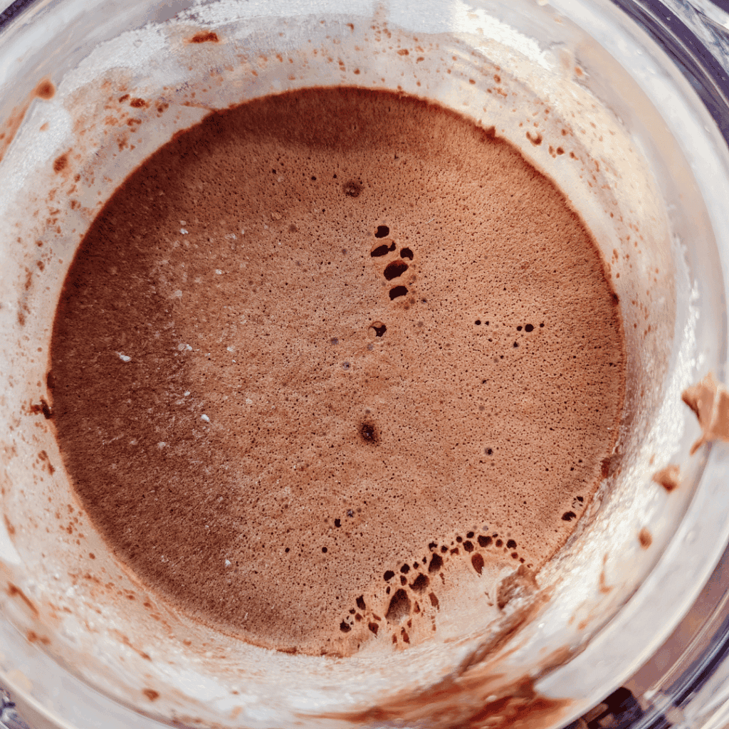 Chocolate hot cocoa mix in a glass jar with a spoon.