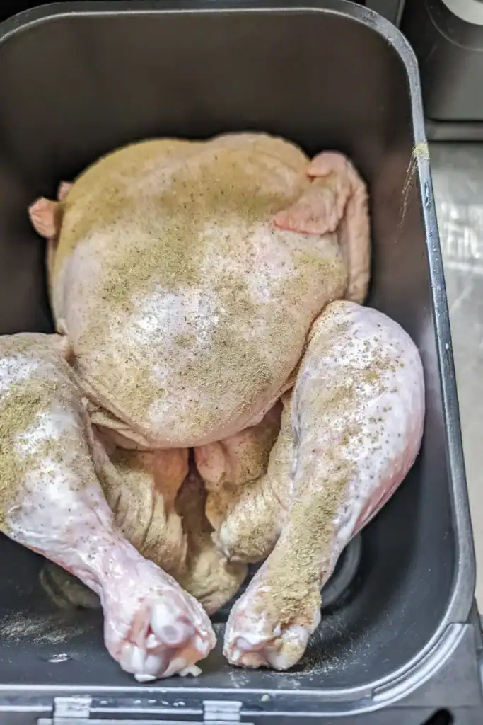 whole chicken in air fryer basket with poultry seasoning