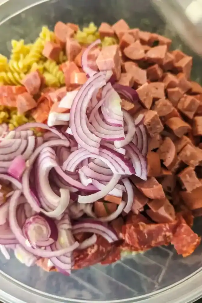 adding thin sliced red onion to the pasta salad