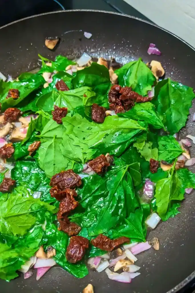 adding sun-dried tomato on top of the wilted lambsquarters in fry pan
