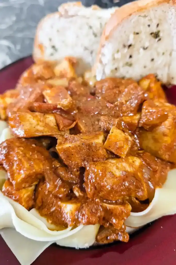 butter chicken pasta served on red trimmed plate with two pieces garlic bread