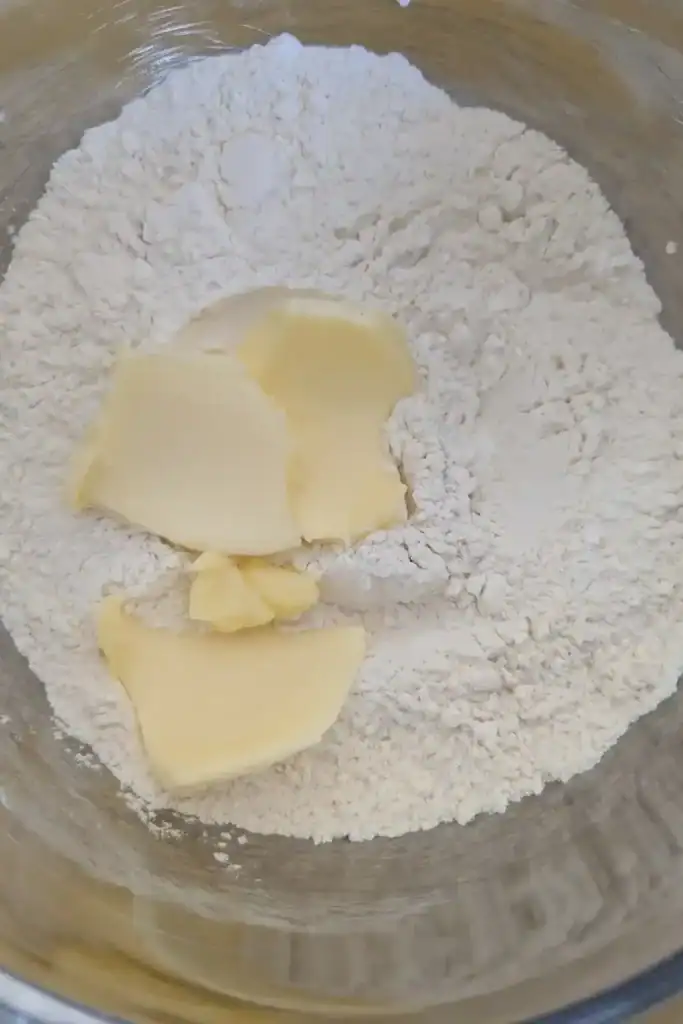 adding cold butter to the dry ingredients in the biscuit dough in a stainless mixing bowl