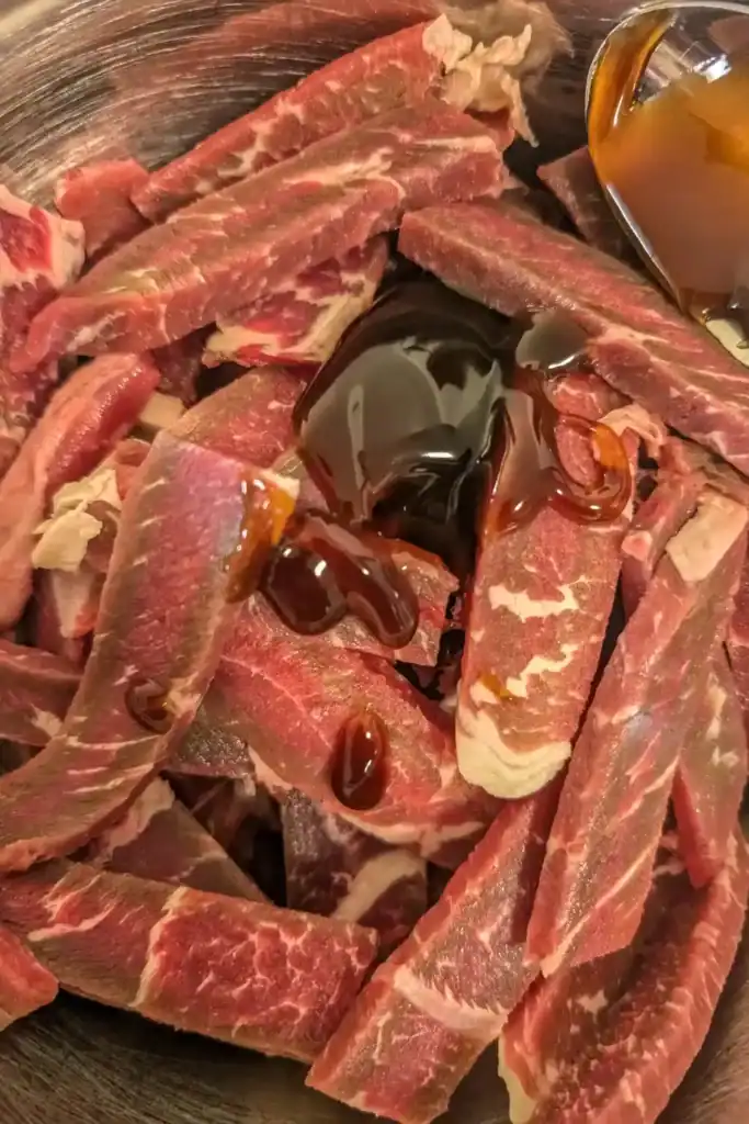 adding marinade ingredients to raw beef strips in bowl