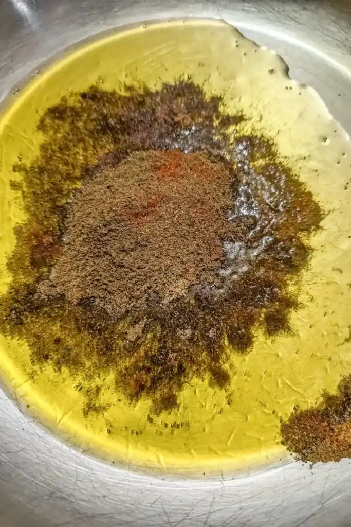 adding Indian spices to heated ghee in stainless steel saute pan