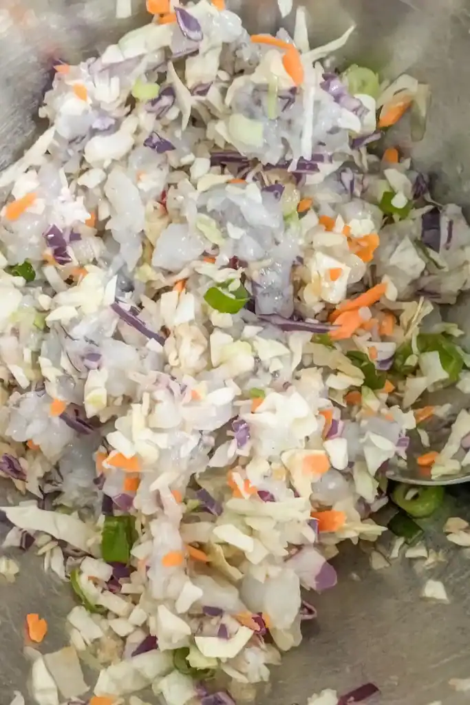 adding the sauces and seasoning to spring roll filling in stainless steel bowl