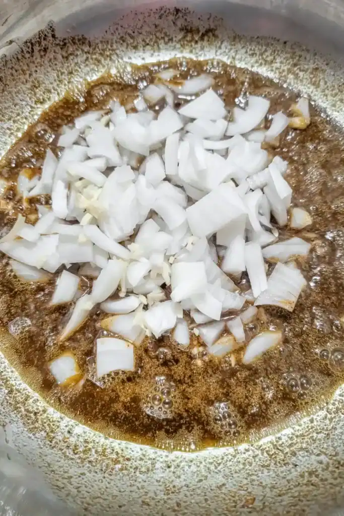 adding diced onion to spiced ghee in stainless steel saute pan