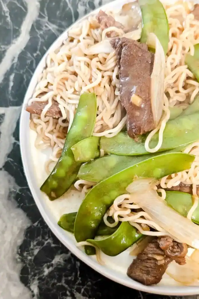 the ginger beef and snow pea with noodle dish as seen from above edge of plate. Plate off screen on black marble table