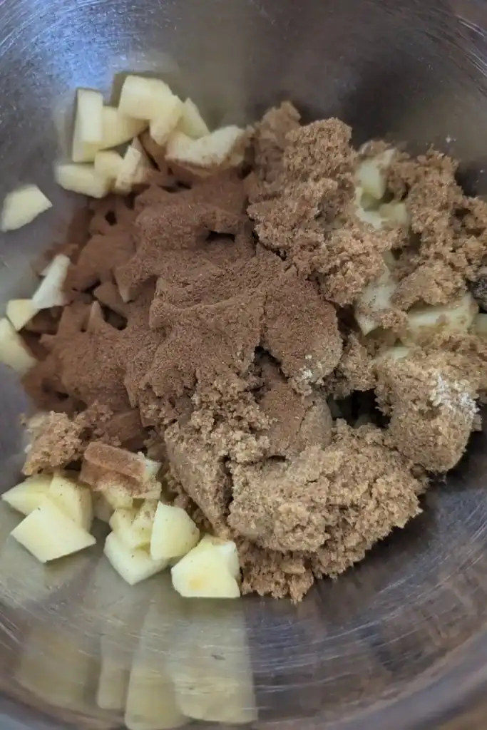 adding cinnamon and brown sugar to the diced apple pieces in a stainless steel bowl