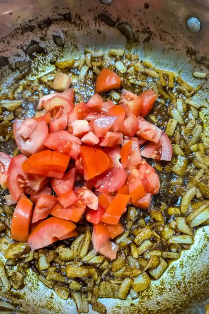 adding chopped tomato to onion spices in saute pan