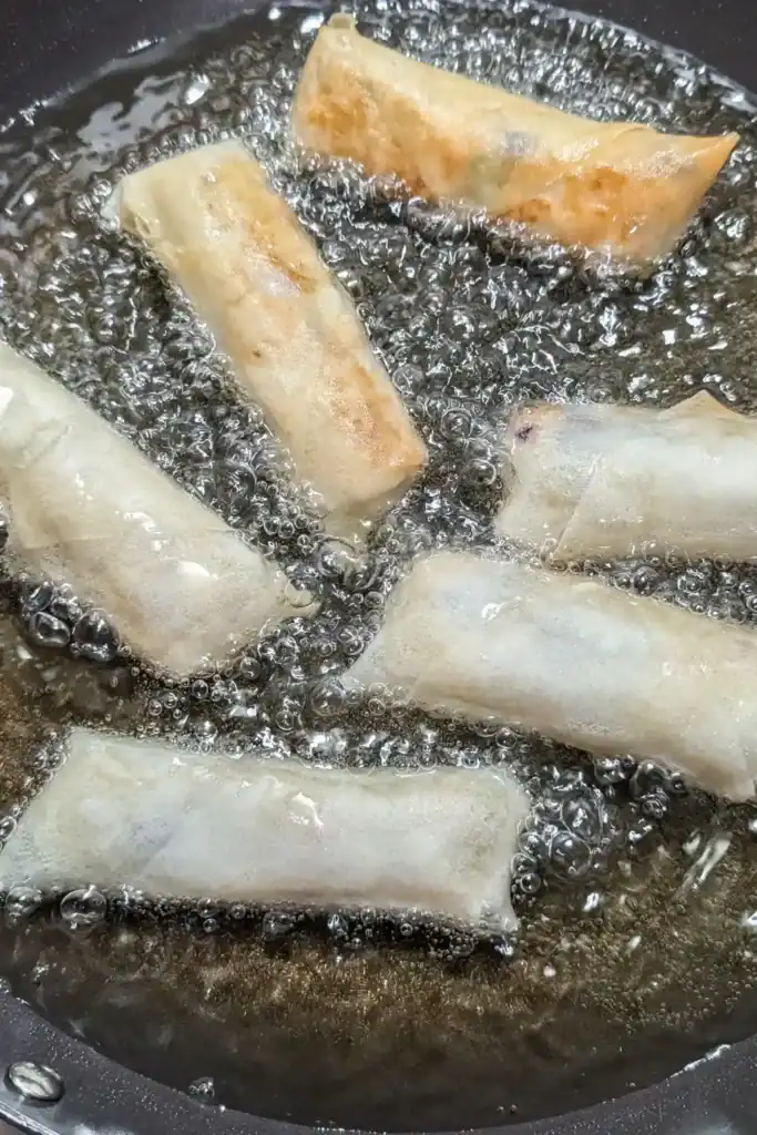 cooking the spring rolls in frying pan with hot oil. Some are turning color and some are still raw looking