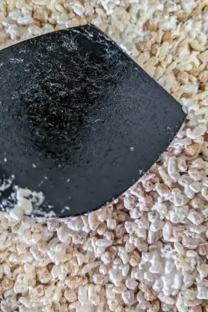 greased back of spatula sits on top of the pressed rice krispie mixture in prepared glass pan