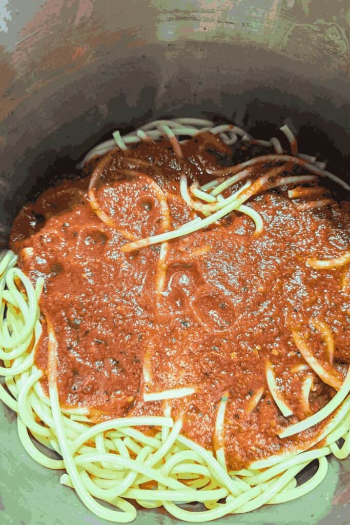 red sauce poured on bucatini noodles in stock pot