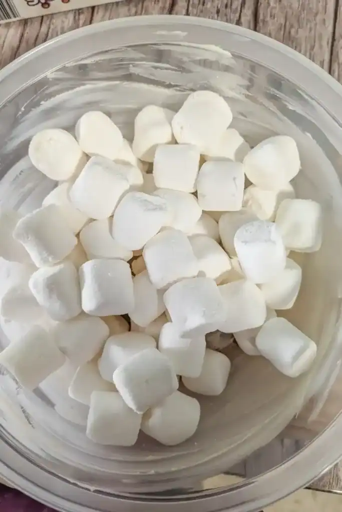 adding large marshmallows to buttered plastic bowl