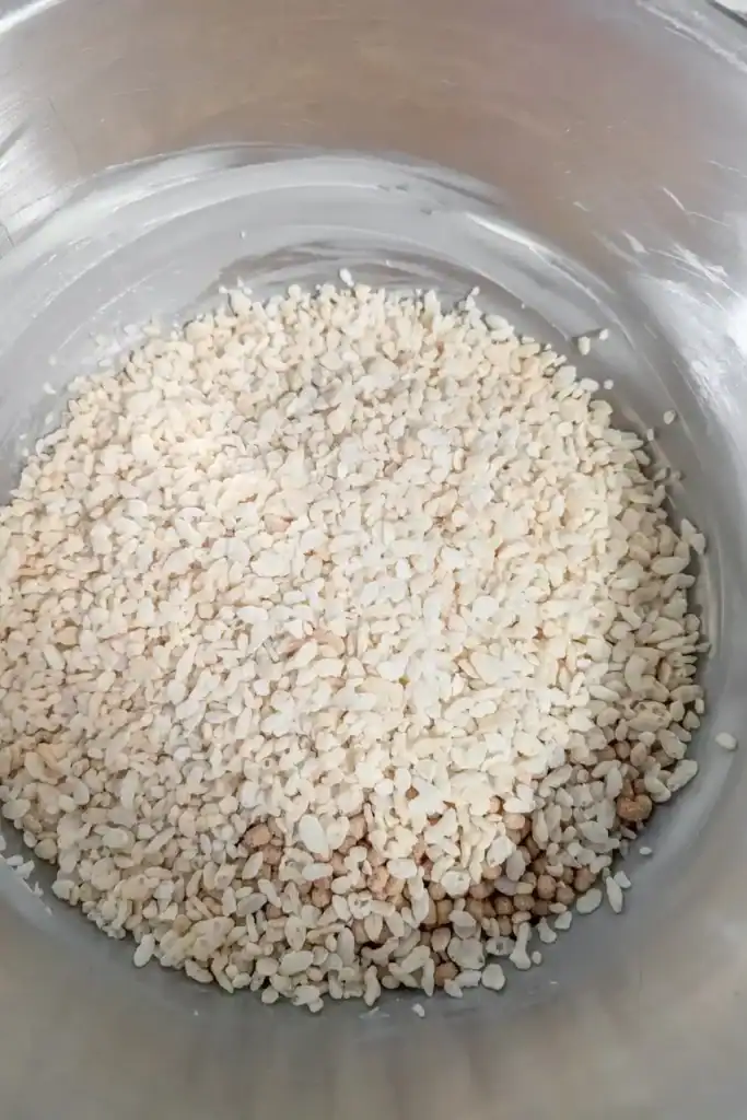 adding rice krispie cereal to the mixture in the stainless steel mixing bowl