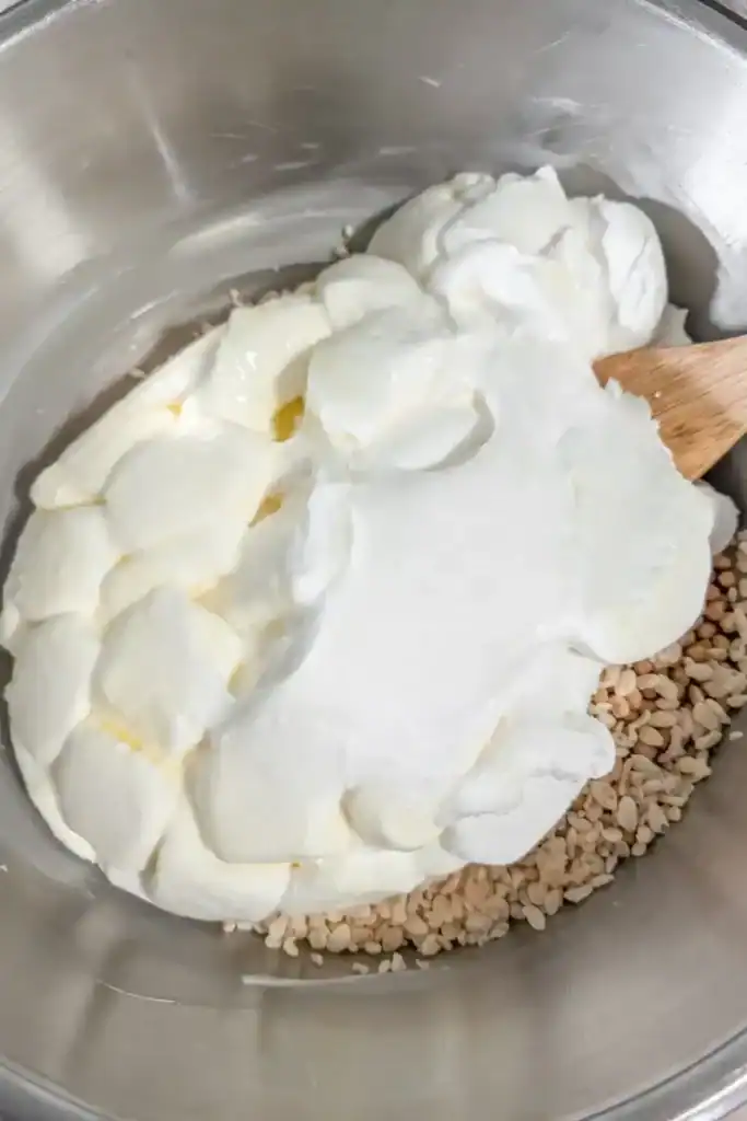 adding the melted marshmallows to the cereal mixture in the stainless steel bowl