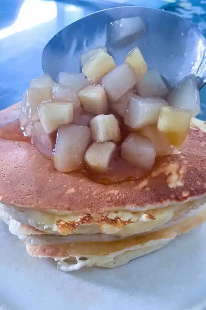 apple cinnamon pear compote being scooped over a stack of pancakes