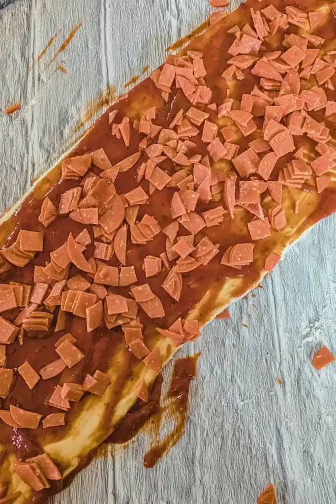 adding diced pepperoni to sauced pizza dough