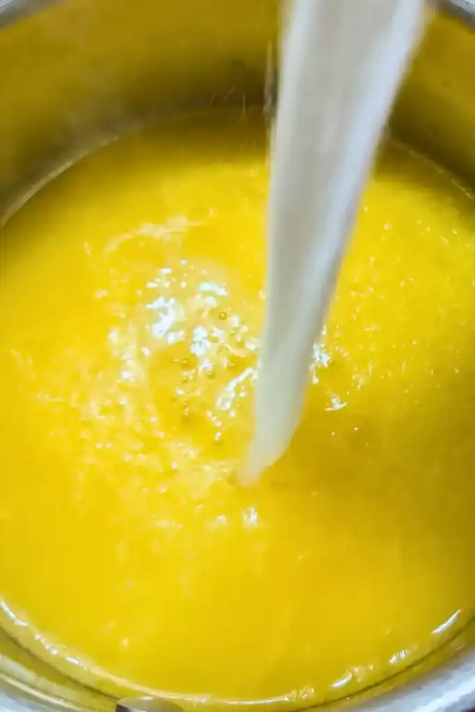 adding cornstarch slurry to hot sweetened orange juice in saucepan