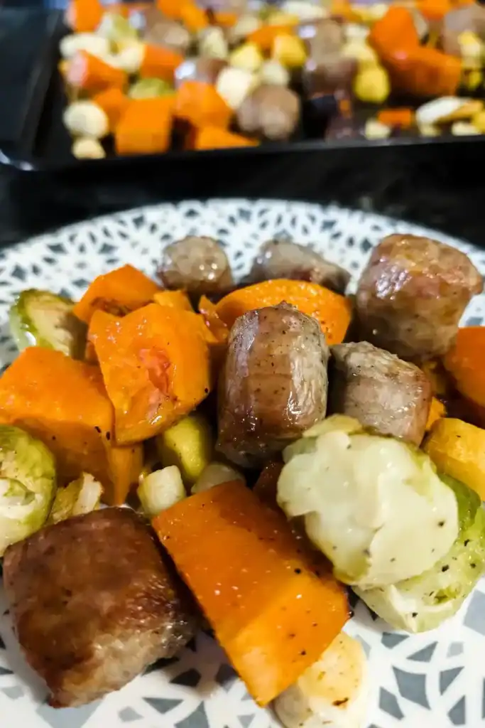 foreground Irish bangers and veg served on blue and white plate in background part of the sheet pan with veg