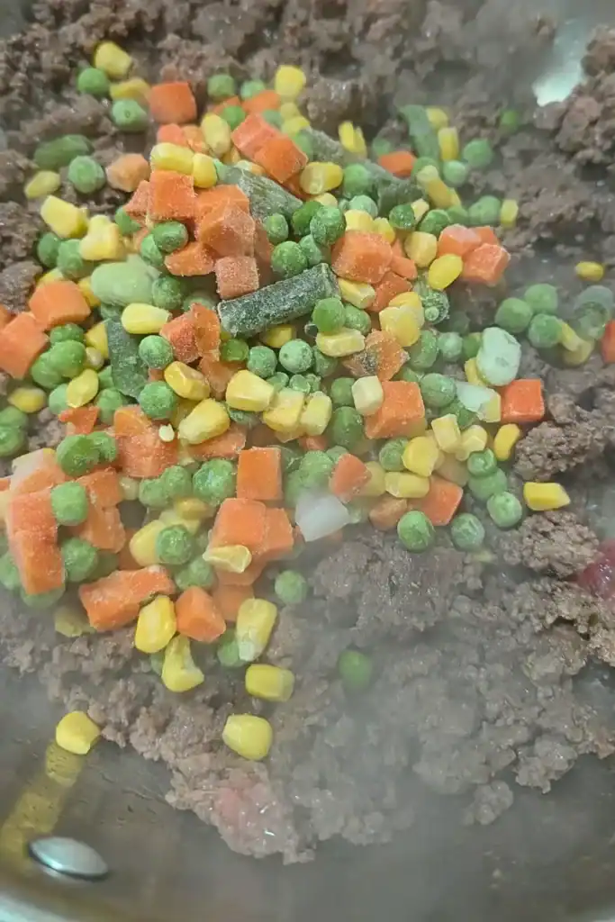 adding frozen mixed vegetables to ground beef in skillet