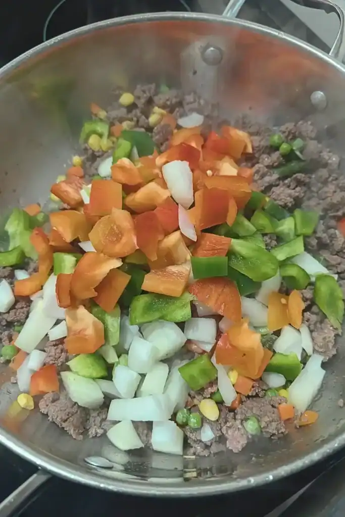 adding the bell peppers and onion to the meat mixture in frying pan