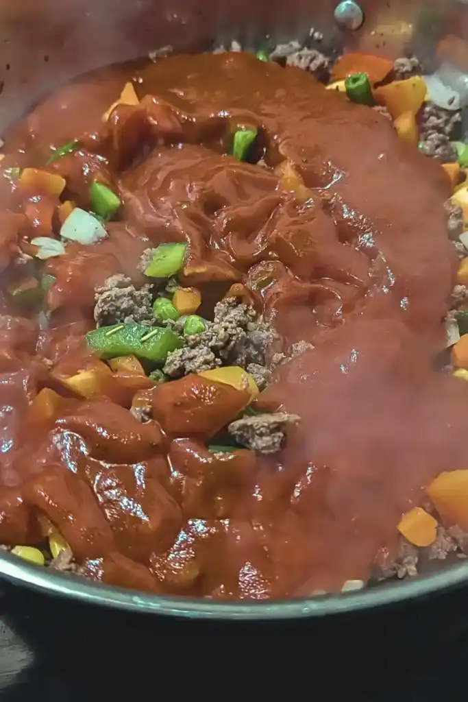 adding the tomato sauce to the meat mixture in frying pan