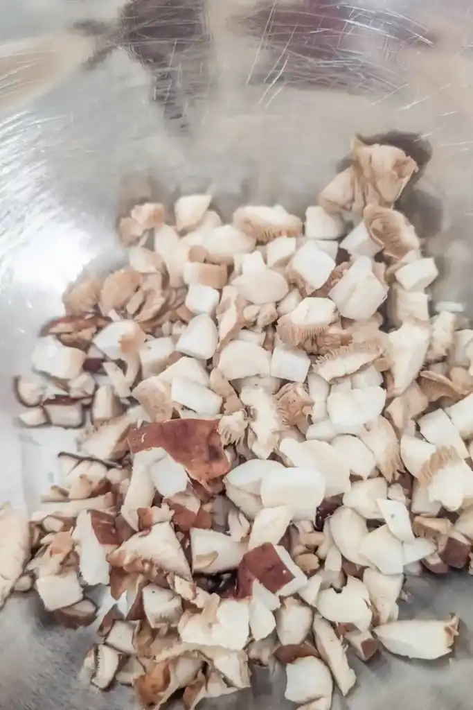 shiitake and baby king oyster mushrooms chopped in stainless steel bowl