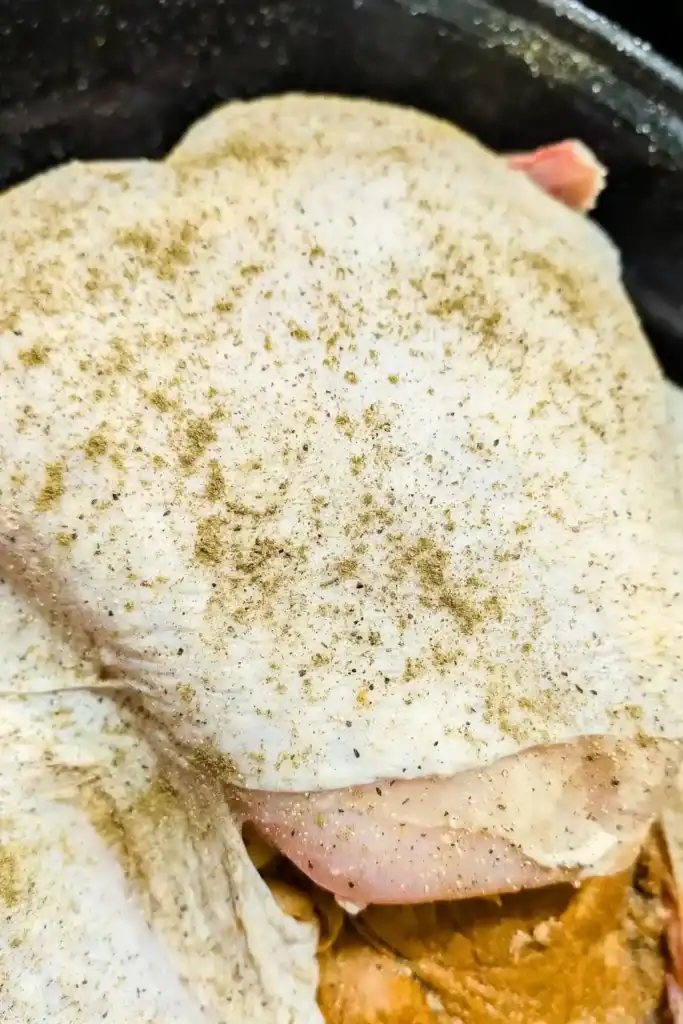 adding poultry seasoning to whole raw turkey with stuffing