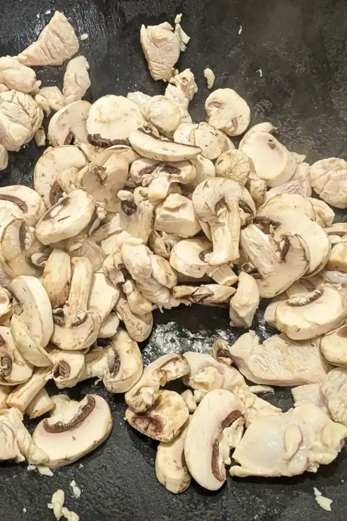 adding sliced white mushrooms to the chicken in the wok