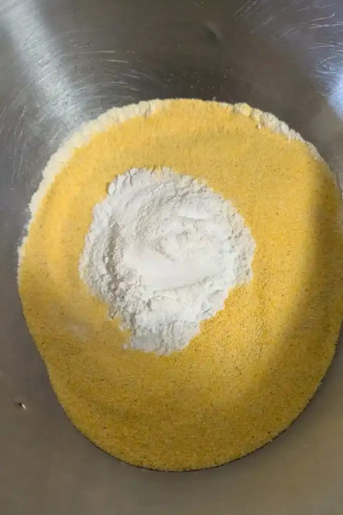 adding cornmeal to flour in stainless steel bowl for cornbread