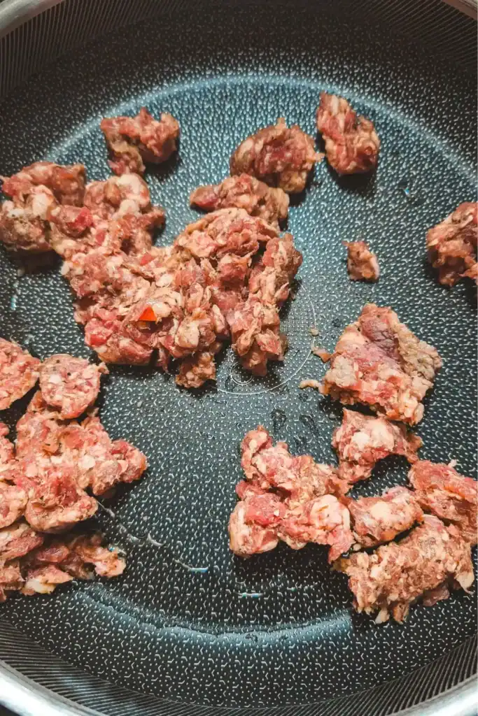 adding raw sausage to the pan with oil