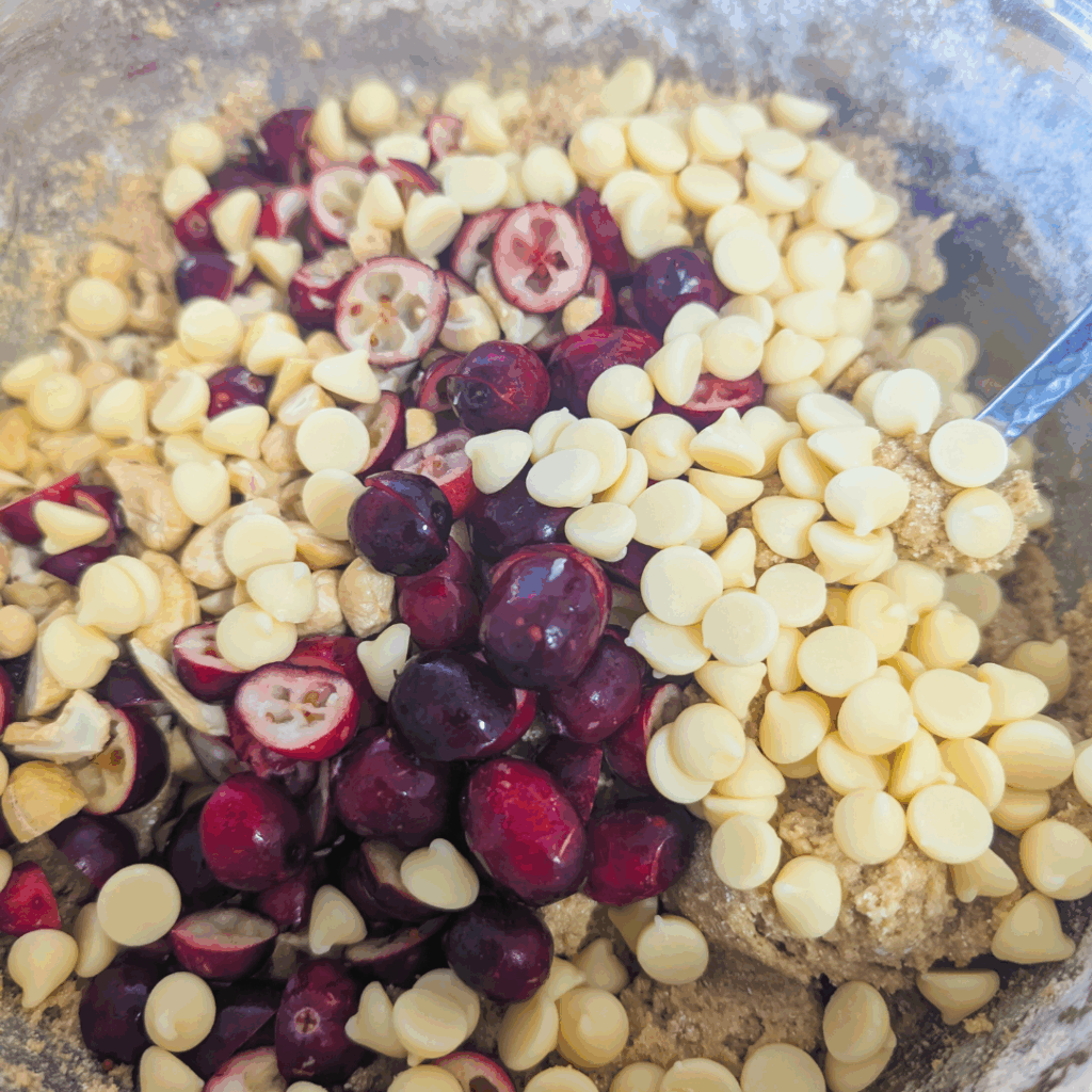 Fresh tart cherries, white chocolate chips, and cookie dough in a mixing bowl for homemade cherry white chocolate chip cookies.