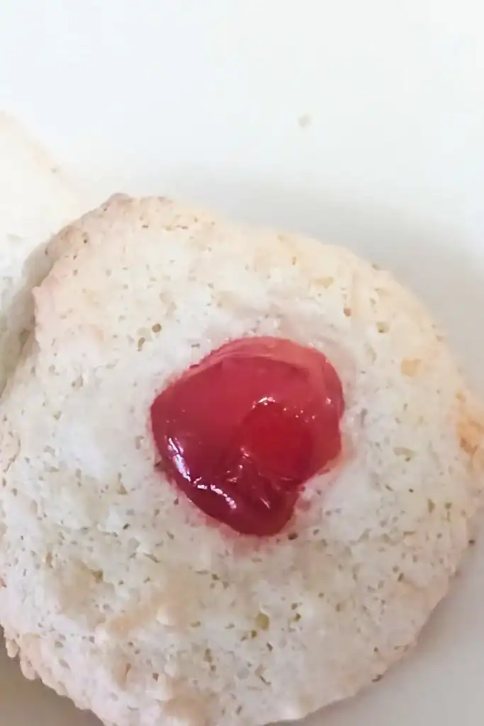 a red cherry sits a top a white coconut macaroon cookie