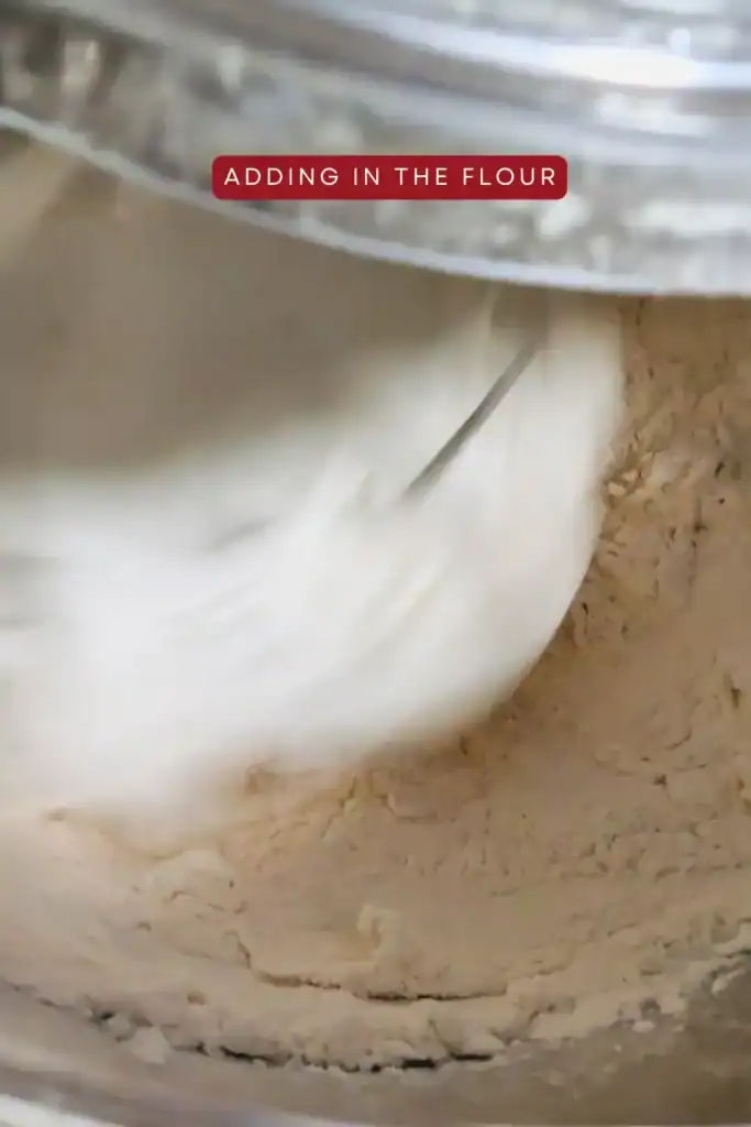 adding flour to the egg white mixture in the stand mixer bowl