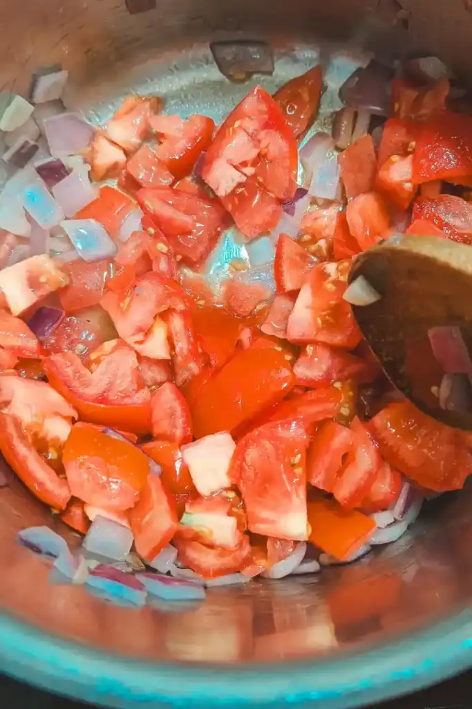 adding chopped tomato to onion and garlic
