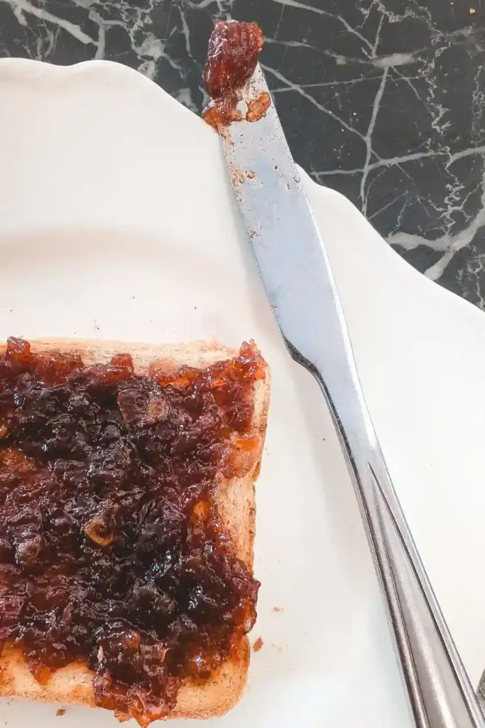 a knife lays on the side of a white plate with apple butter on the blade next to it a piece of toast spread with the apple butter